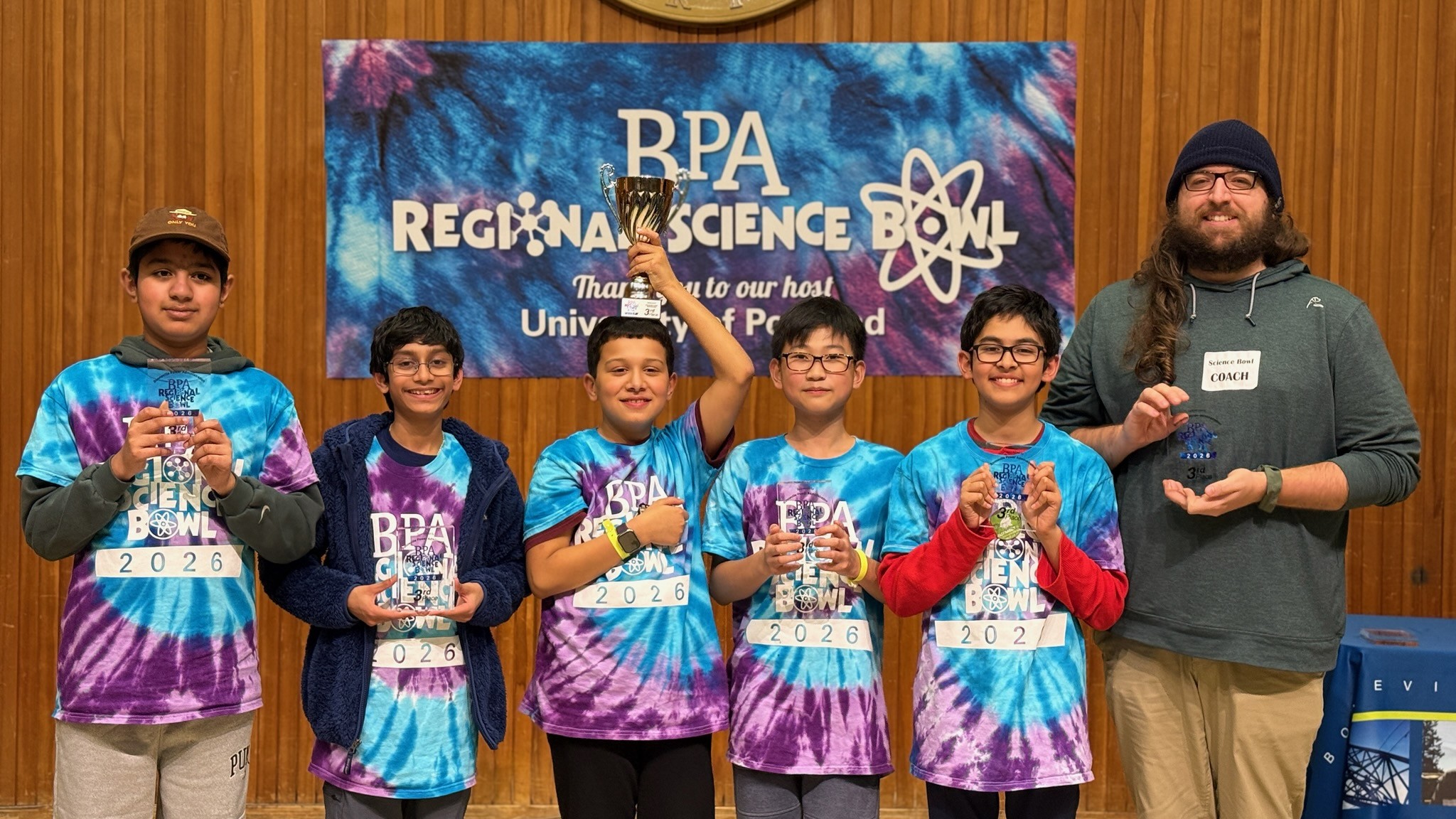 six people standing in a row, one person with a trophy on top of his head