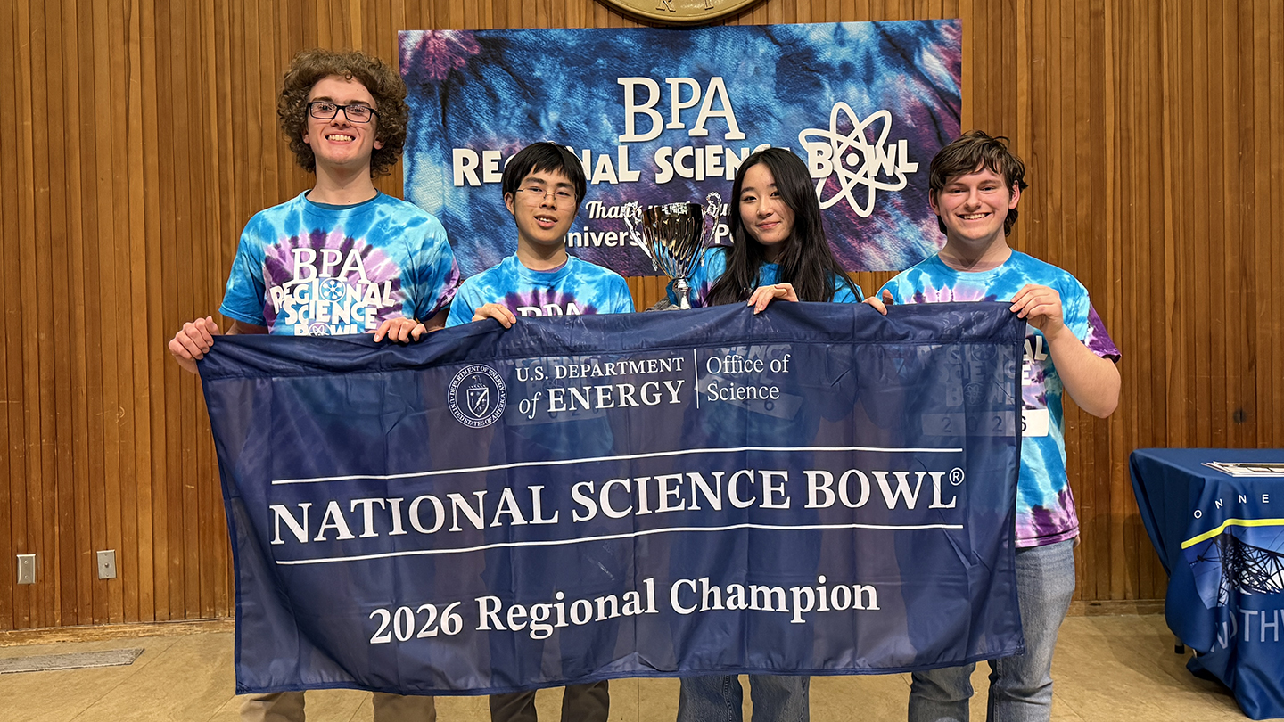 group of people wearing matching science bowl t-shirts, one of which is holding a trophy