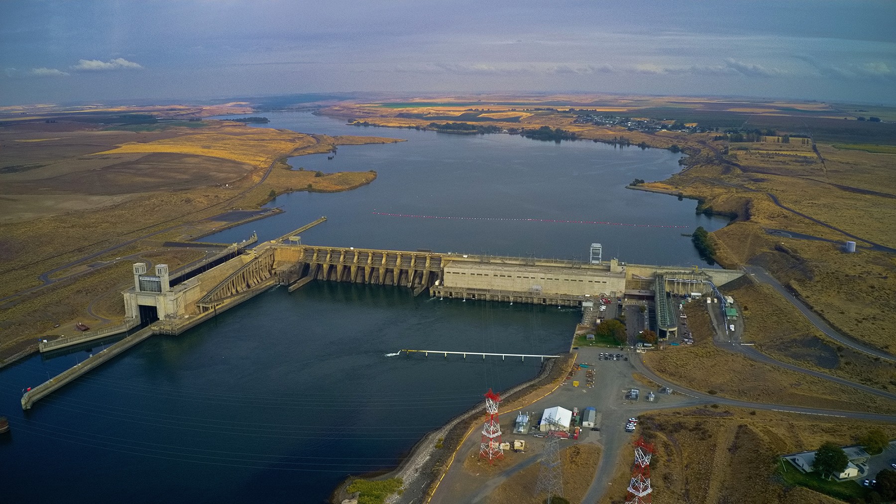 river stretching onto the horizon with olive colored hilly terrain to either side and a concrete structure spanning the water in the foreground