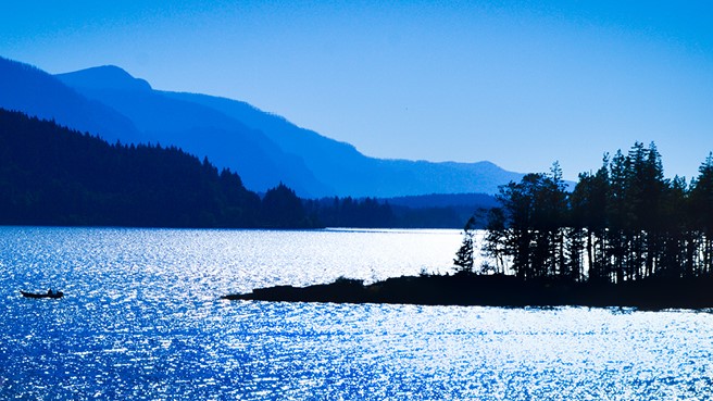 image of river with boat as a silhouette and land with tress jutting out into waterway